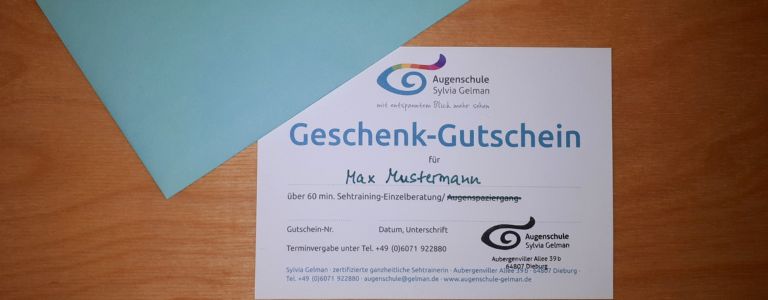 Geschenk-Gutschein im Postkartenformat und türkiser Briefumschlag liegen auf einem Holztisch